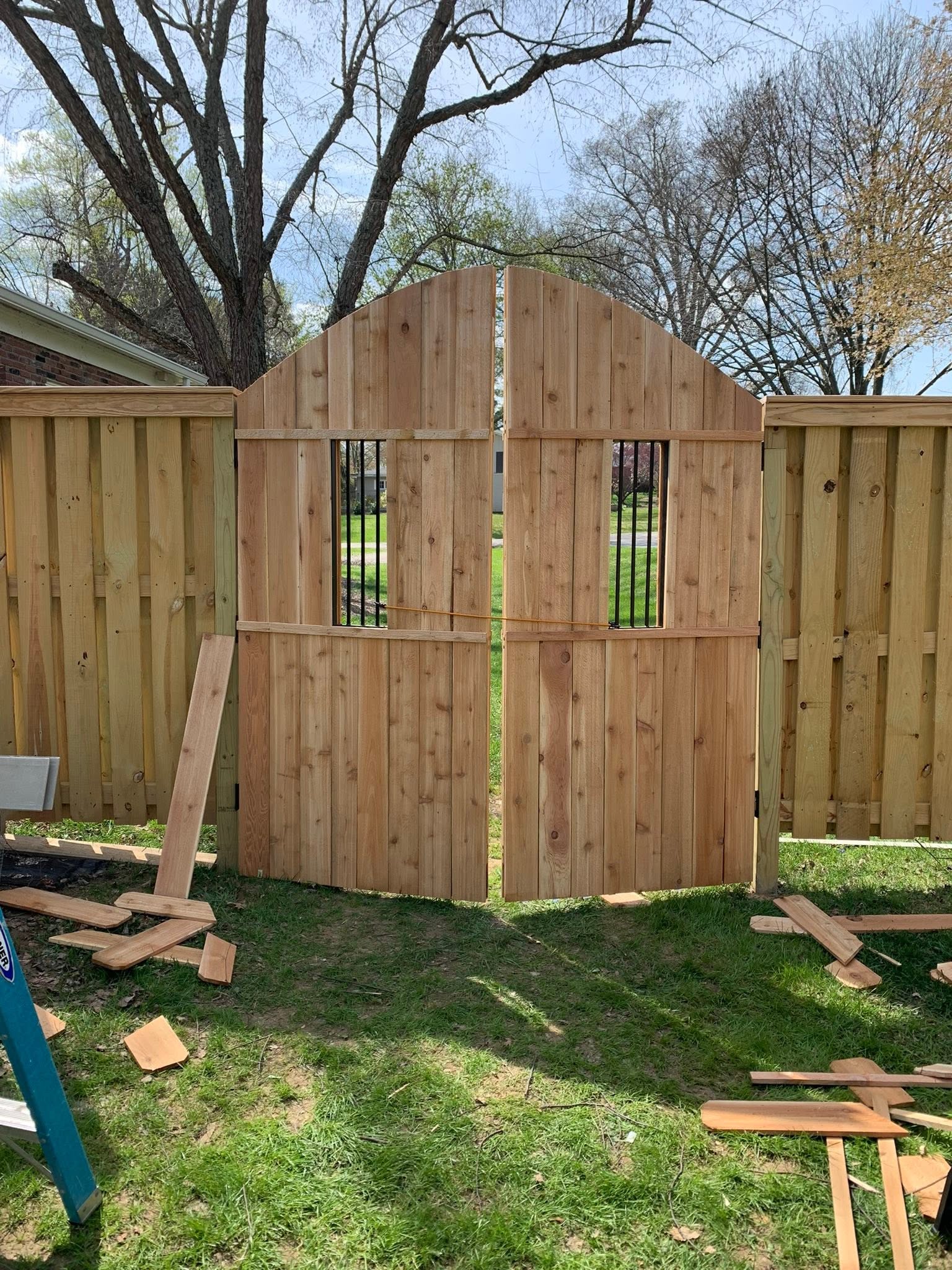 Arched double wood gate with black metal inserts, shown with temporary bracing and offcuts