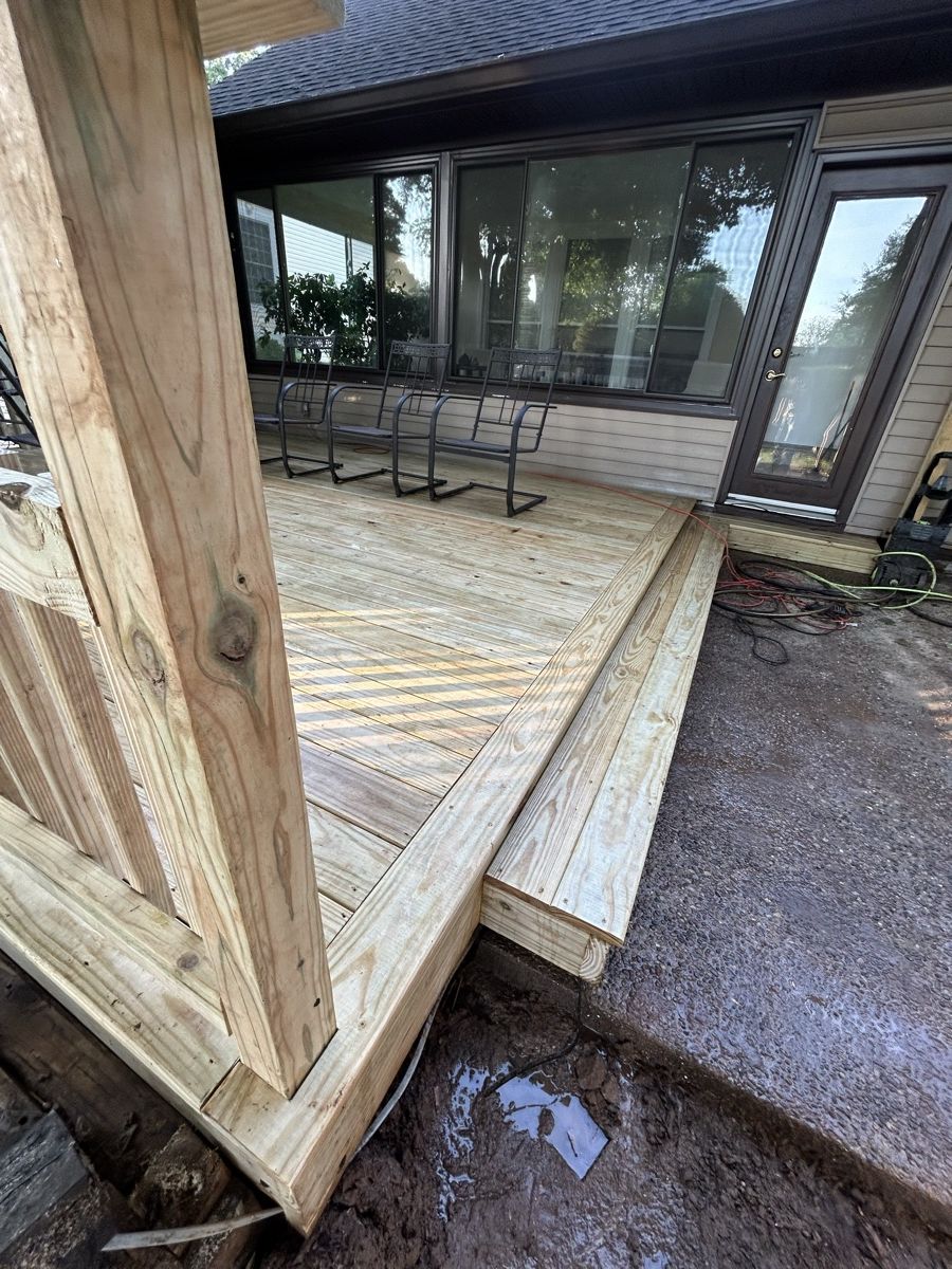 Broad wood step between a low deck and patio beside a light-sided home during construction