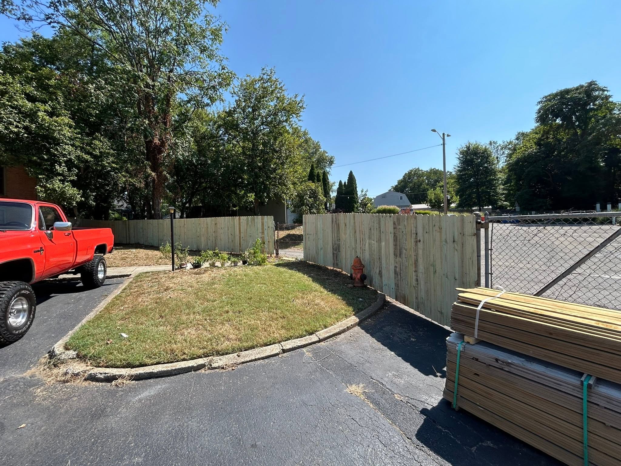 Vertical-board wood privacy fence beside a driveway and garden, with stacked materials nearby