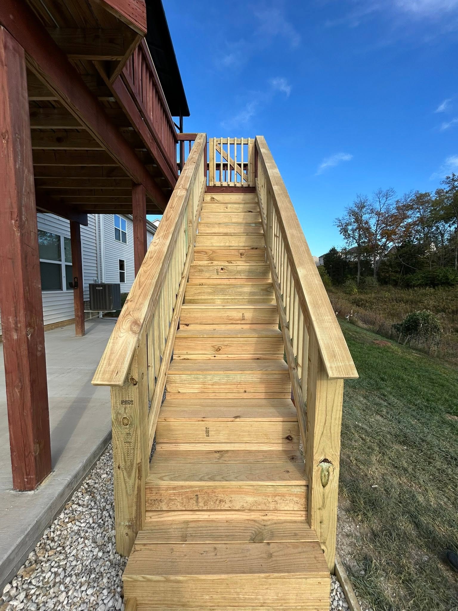 Timber exterior staircase with wood handrails and a gate at the elevated deck landing