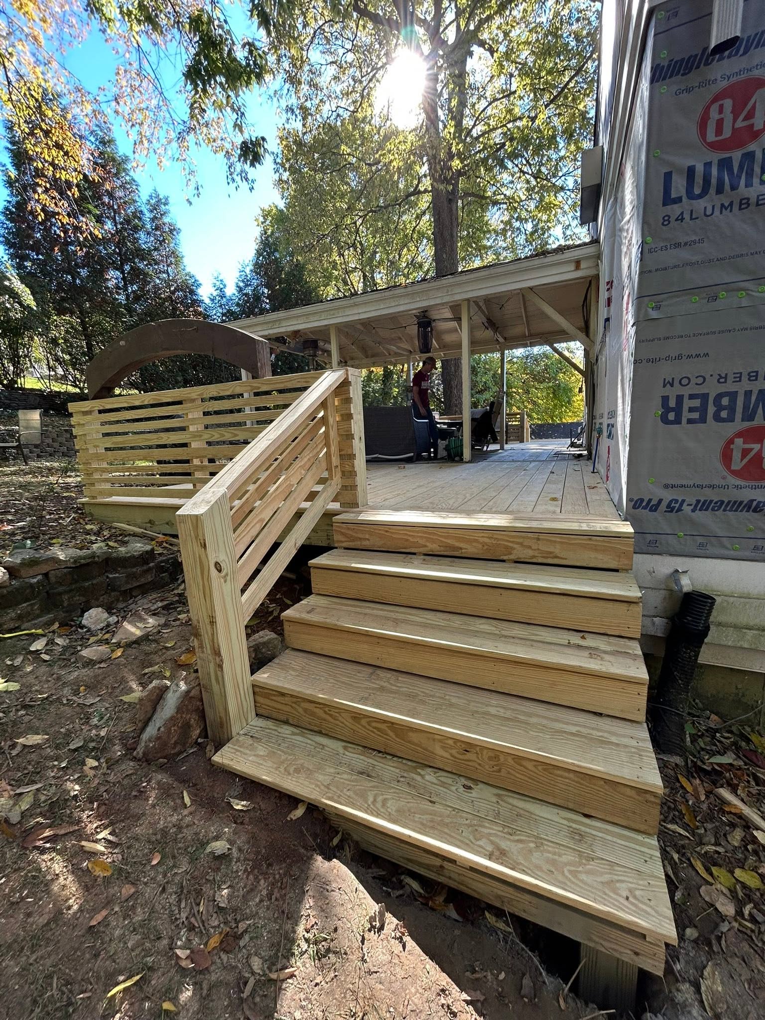 Wood entry steps and horizontal-slat railings beside a home with exposed housewrap