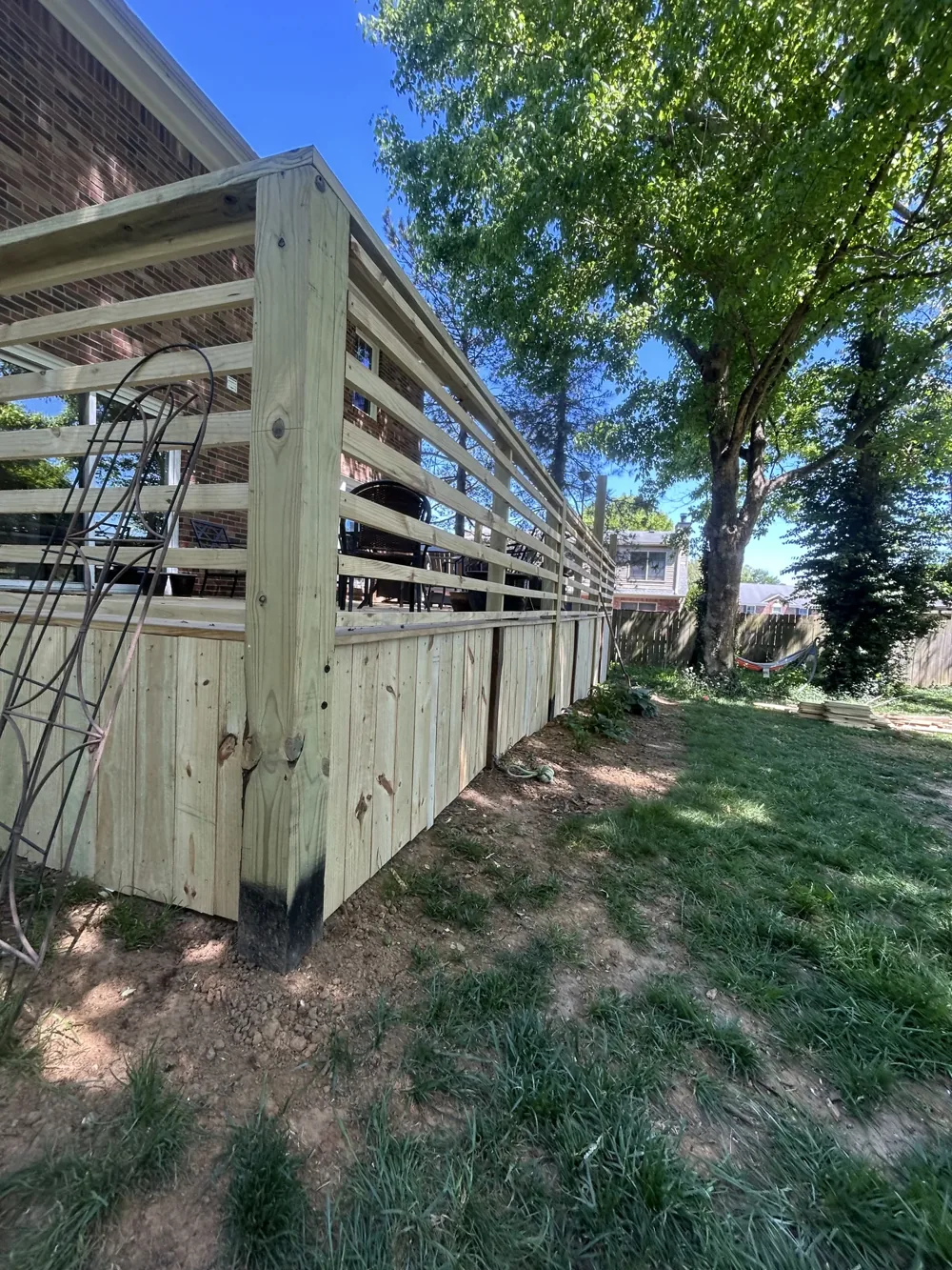 Horizontal timber deck railings and vertical wood skirting beside a leafy yard