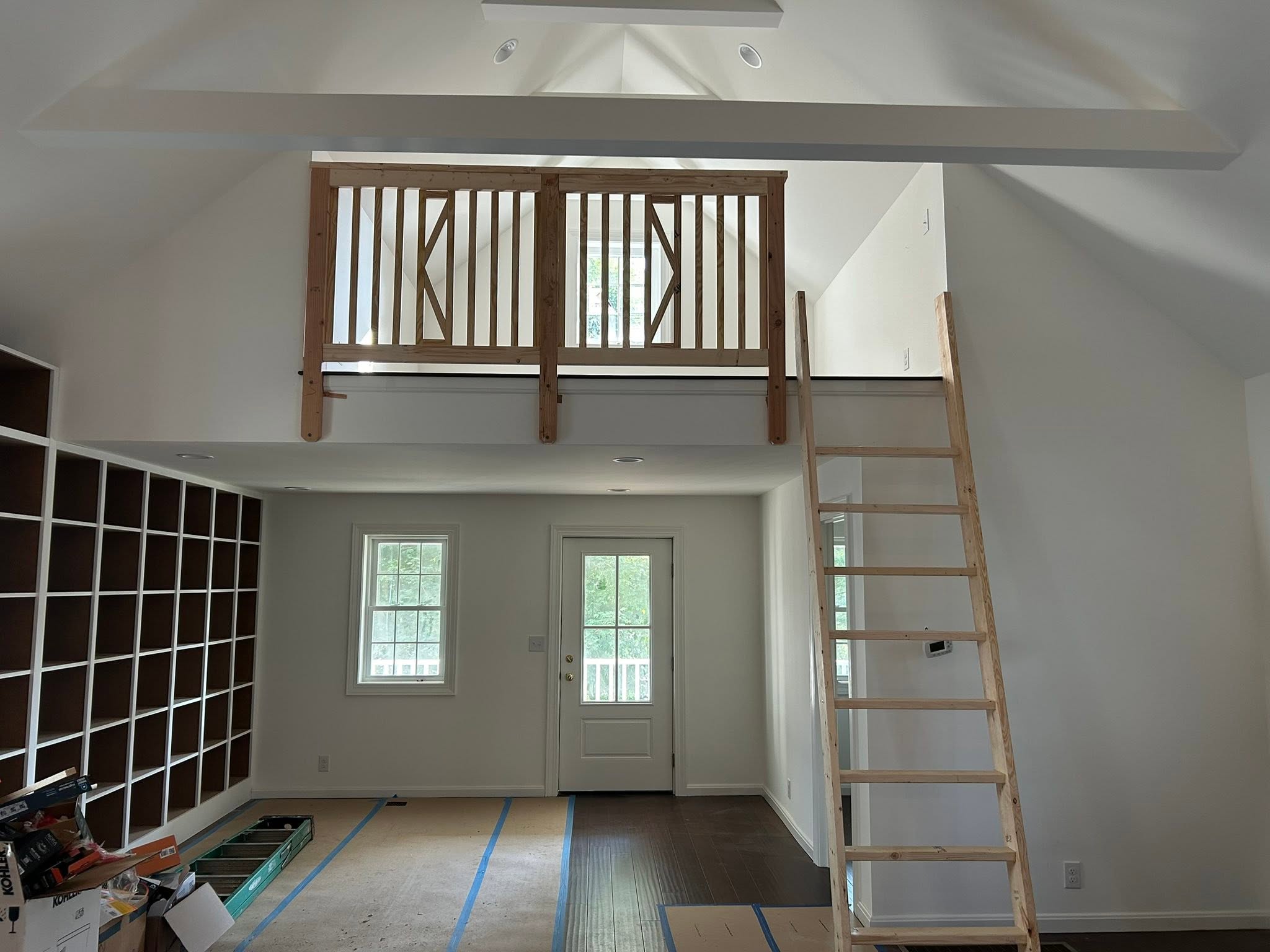 Wood loft railing and ladder inside a home with protective floor covering and construction materials