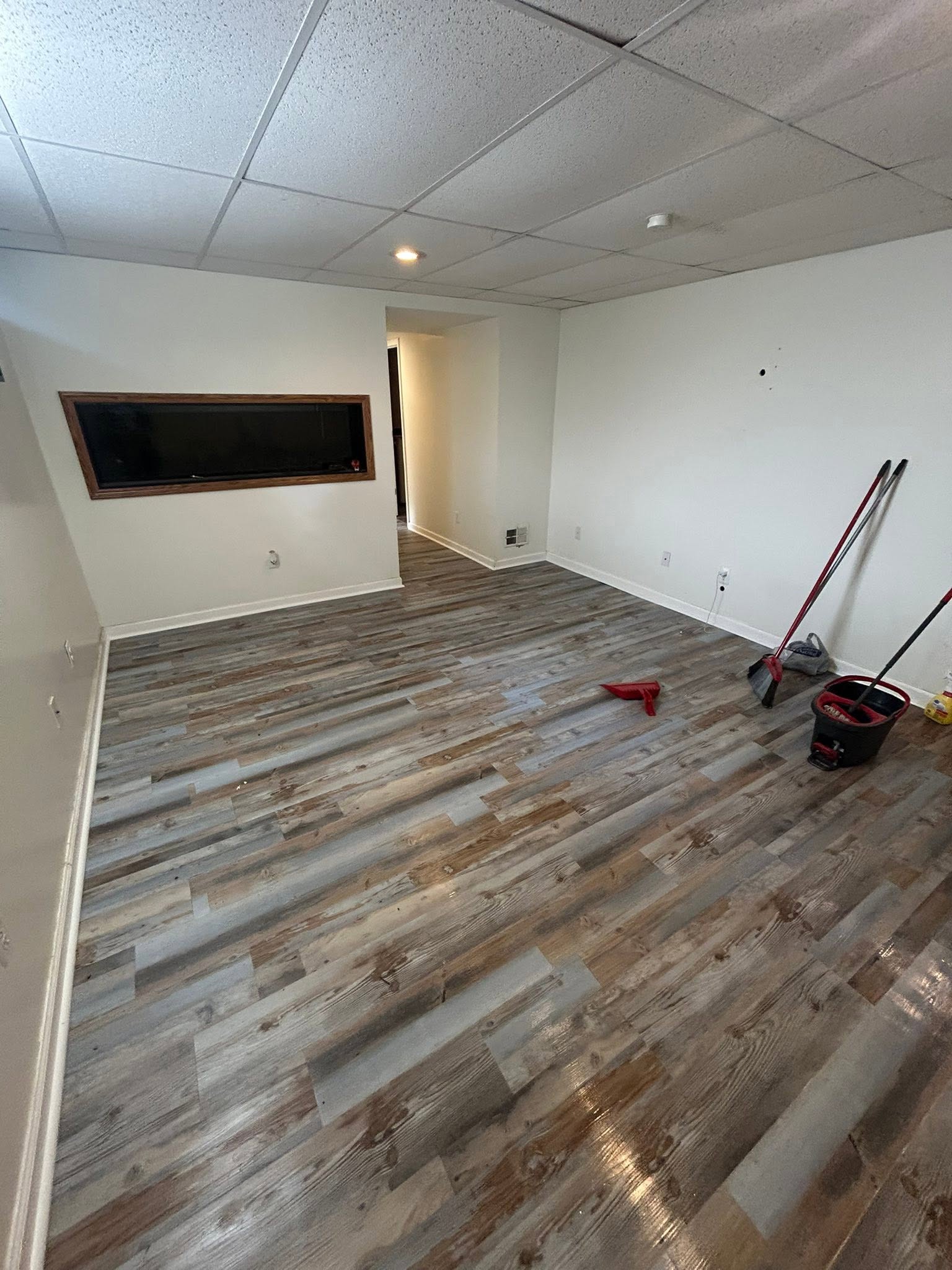 Interior room with wood-look plank flooring, white baseboards and cleaning equipment