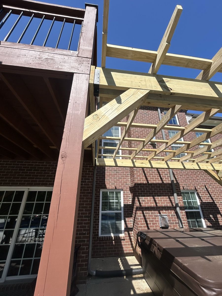Close view of a diagonal wood brace, beam and rafters on a pergola beside an existing raised deck