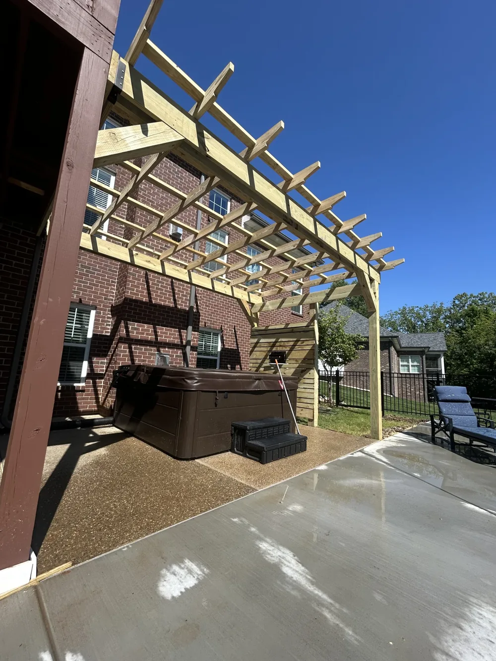 A timber pergola shading a hot tub beside a brick home