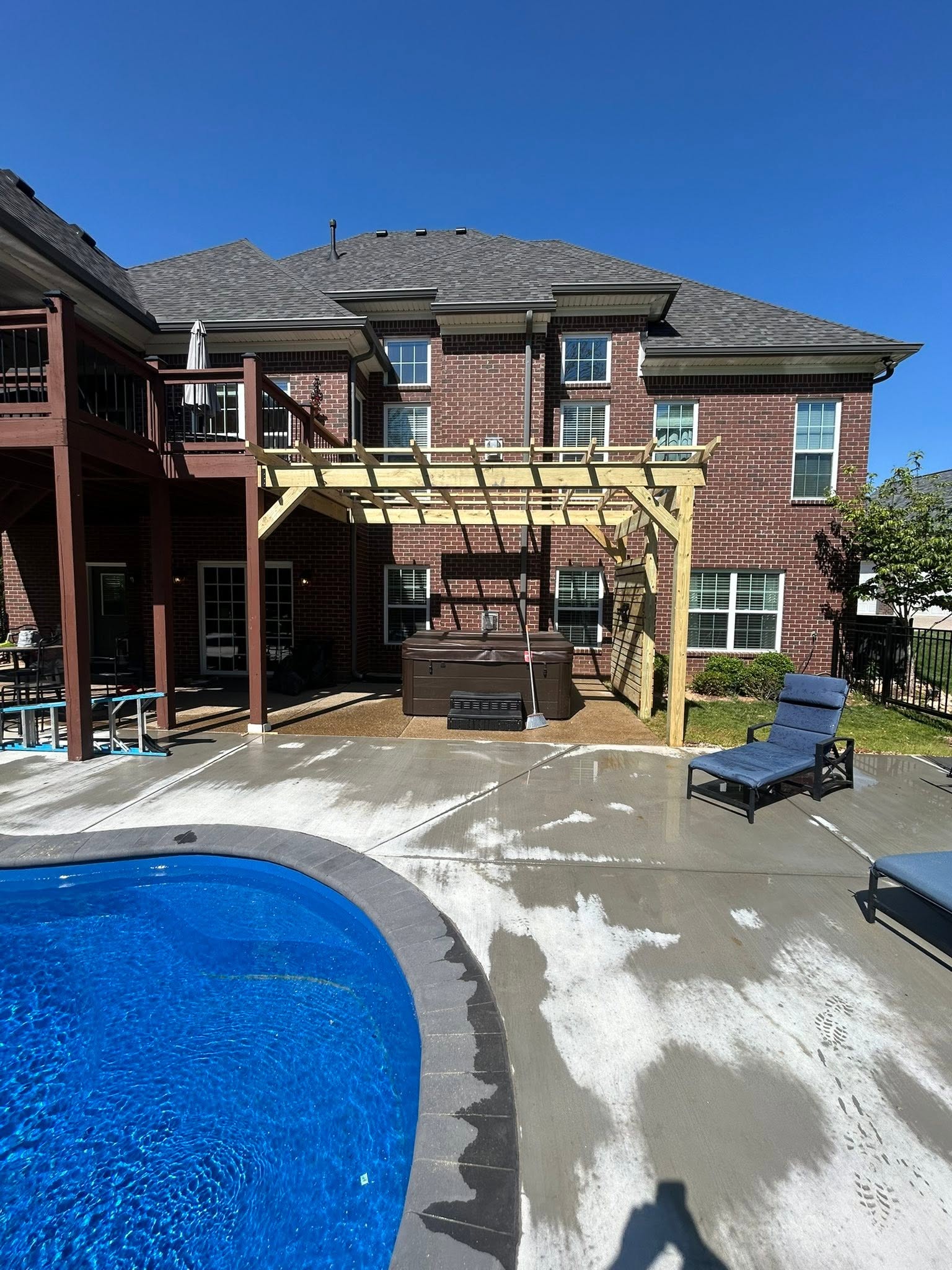 Front view of a timber pergola over a hot tub beside a brick home and backyard pool