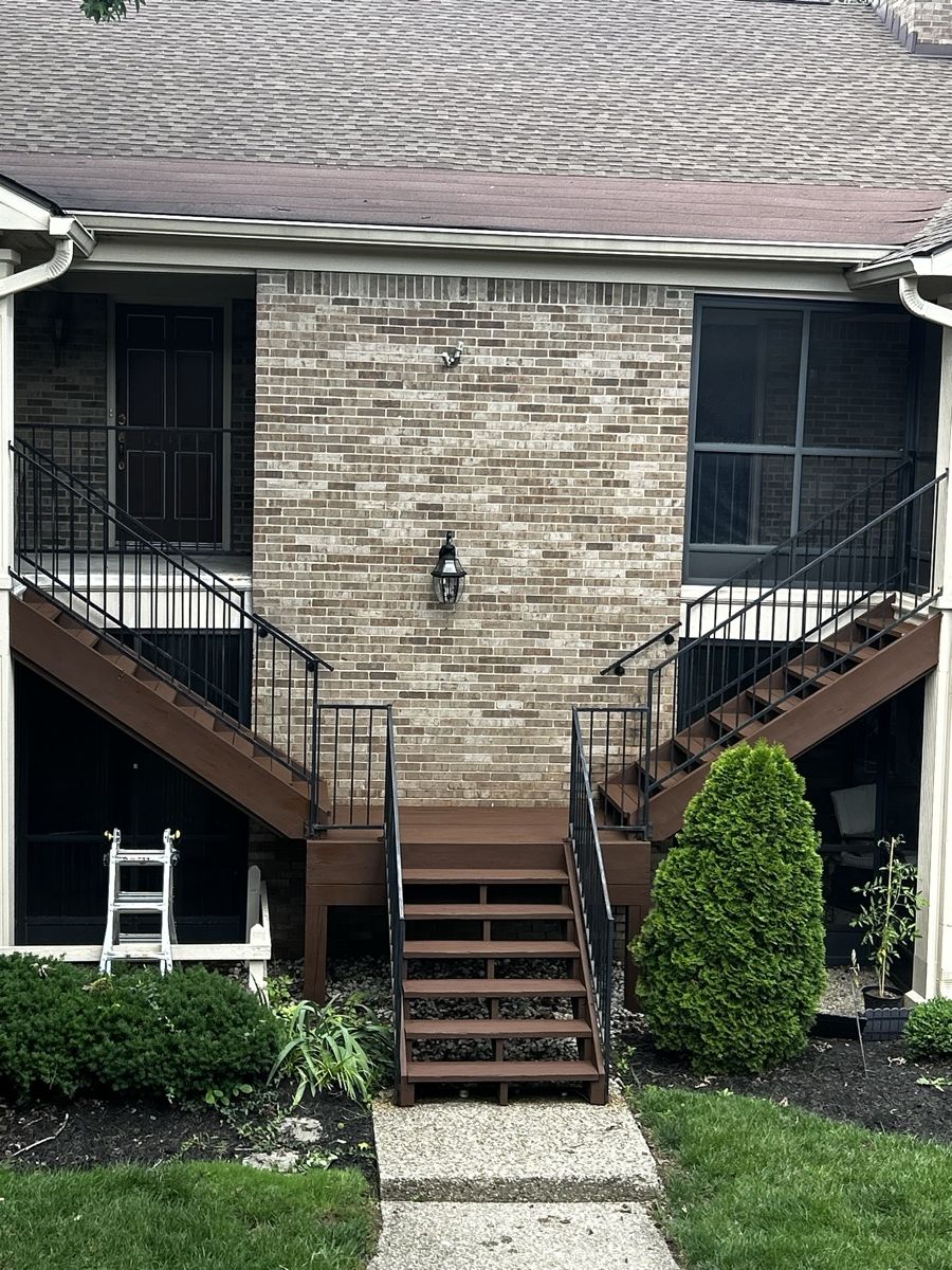 Split exterior staircase with a shared landing and black railings behind a brick home