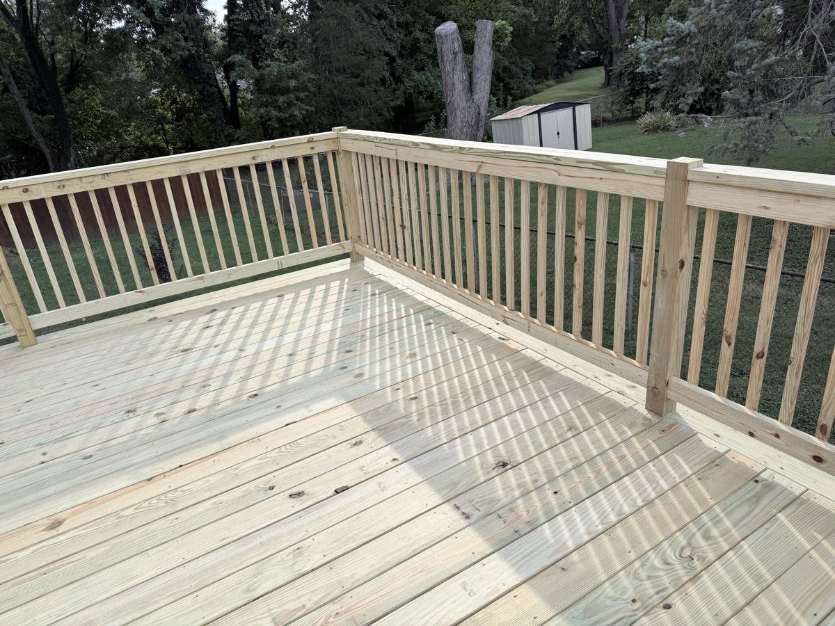A wood deck corner with matching railings and vertical balusters overlooking a backyard